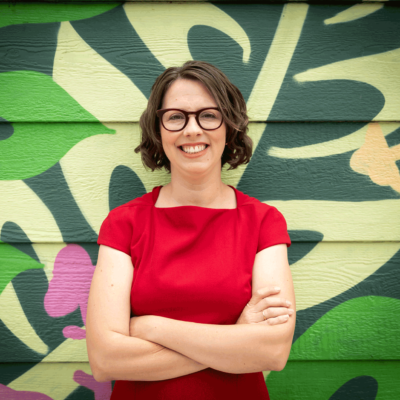 carly_solo_red_square image of Carly Stadium-Liang standing in front of a mural in Oakland California